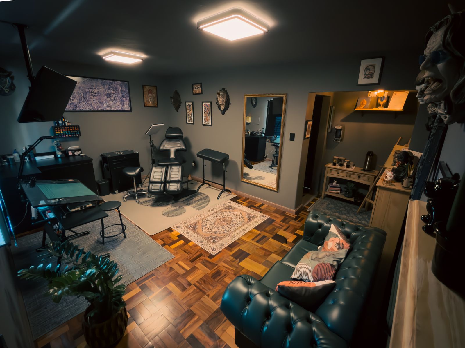 Sala do estúdio com maca, sofá de couro verde, tapetes e quadros nas paredes
